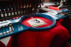 Couture de broderie machine en action sur un tissu rouge, création de logo personnalisé.