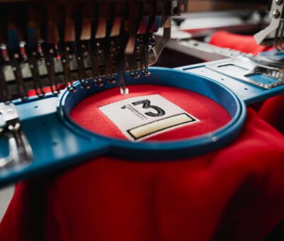 Couture de broderie machine en action sur un tissu rouge, création de logo personnalisé.