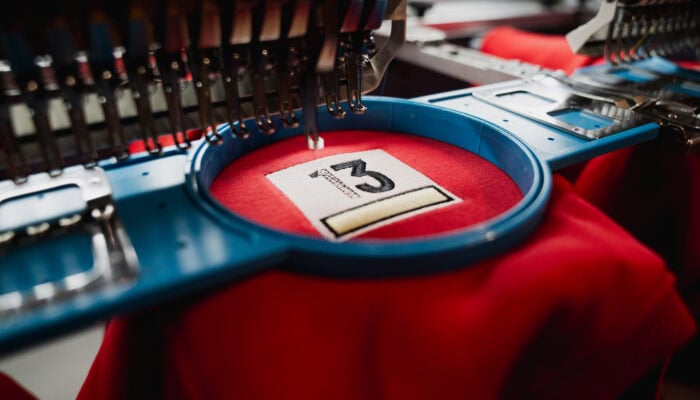 Couture de broderie machine en action sur un tissu rouge, création de logo personnalisé.